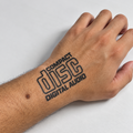 A close-up of a person's hand and wrist showing a temporary tattoo or decal that reads 'COMPACT disc DIGITAL AUDIO' in black outline lettering, placed on a light gray background.