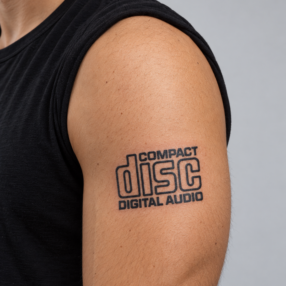 A close-up of a man's upper arm and shoulder wearing a black tank top, featuring a black graphic print that reads 'COMPACT disc DIGITAL AUDIO'.