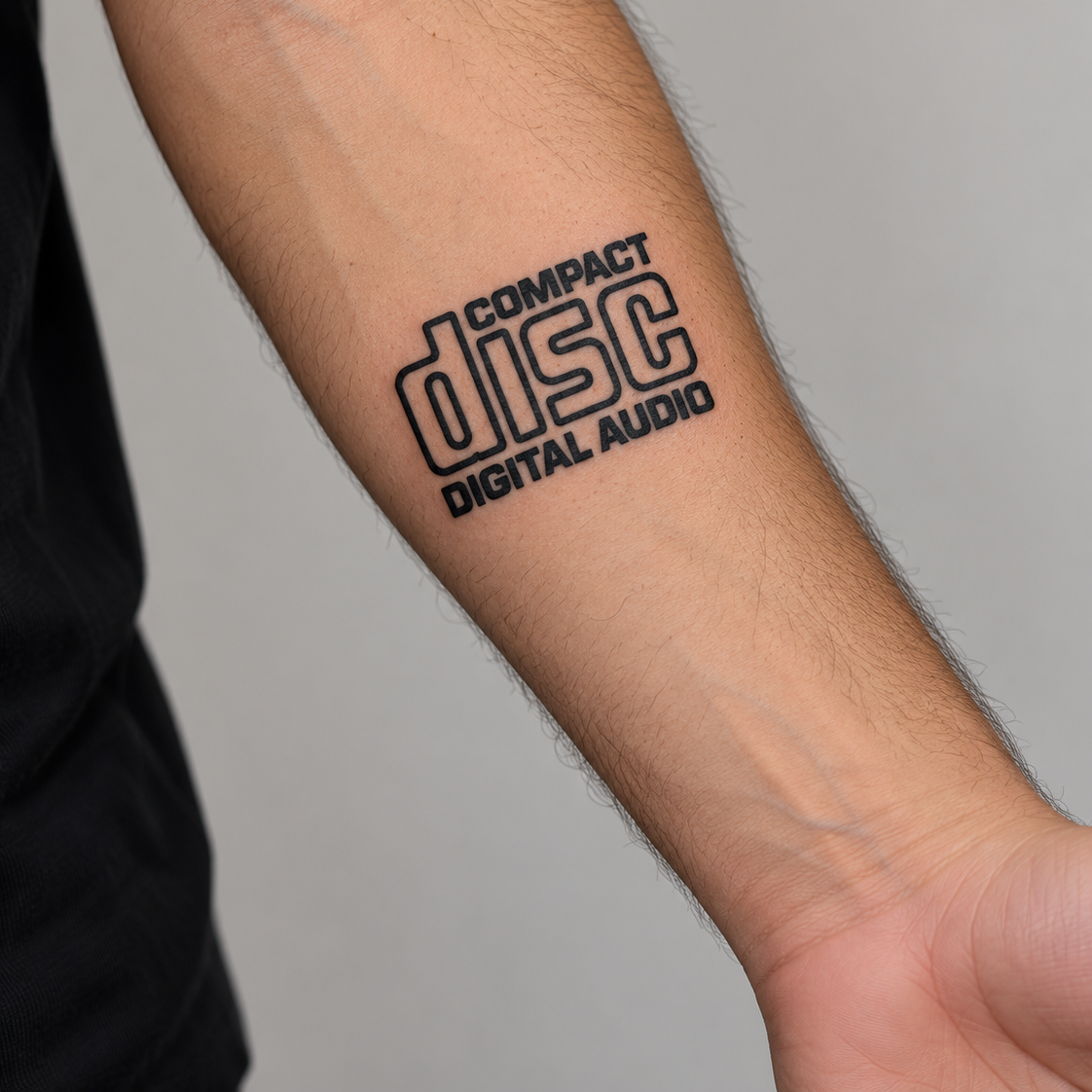 A close-up of a person's forearm featuring a black graphic tattoo of the 'Compact Disc Digital Audio' logo, set against a plain gray background.